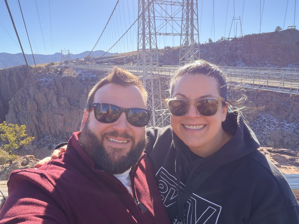 Mike and Amanda smiling together at a suspension bridge over a canyon